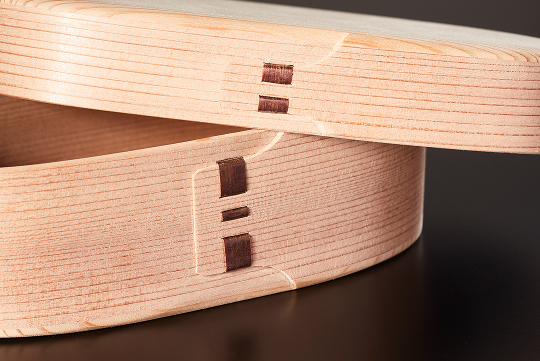 側面を留める「樺綴じ（かばとじ）」が象徴的。桜皮の艶が白木に映え、曲げわっぱならではの表情を生む。